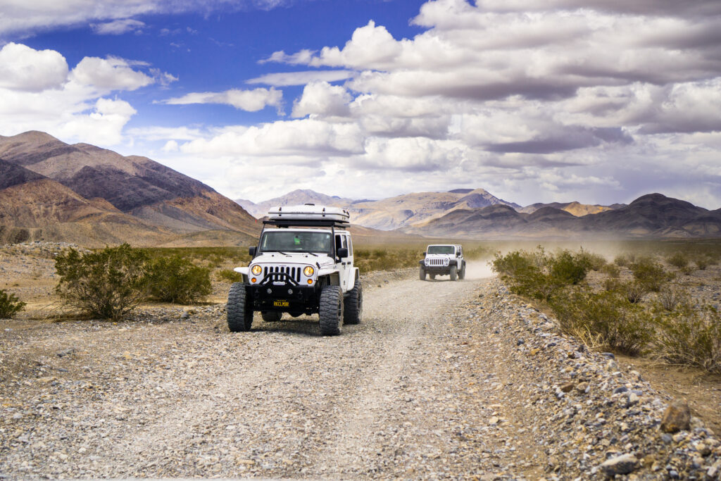 Jeeps driving on dirt road through desert with mountains in the background